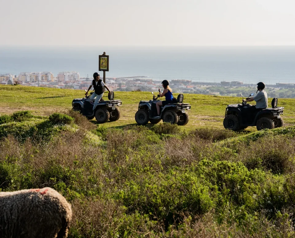 Three quads on a green hilltop overlooking the Costa da Caparica coastline near Lisbon