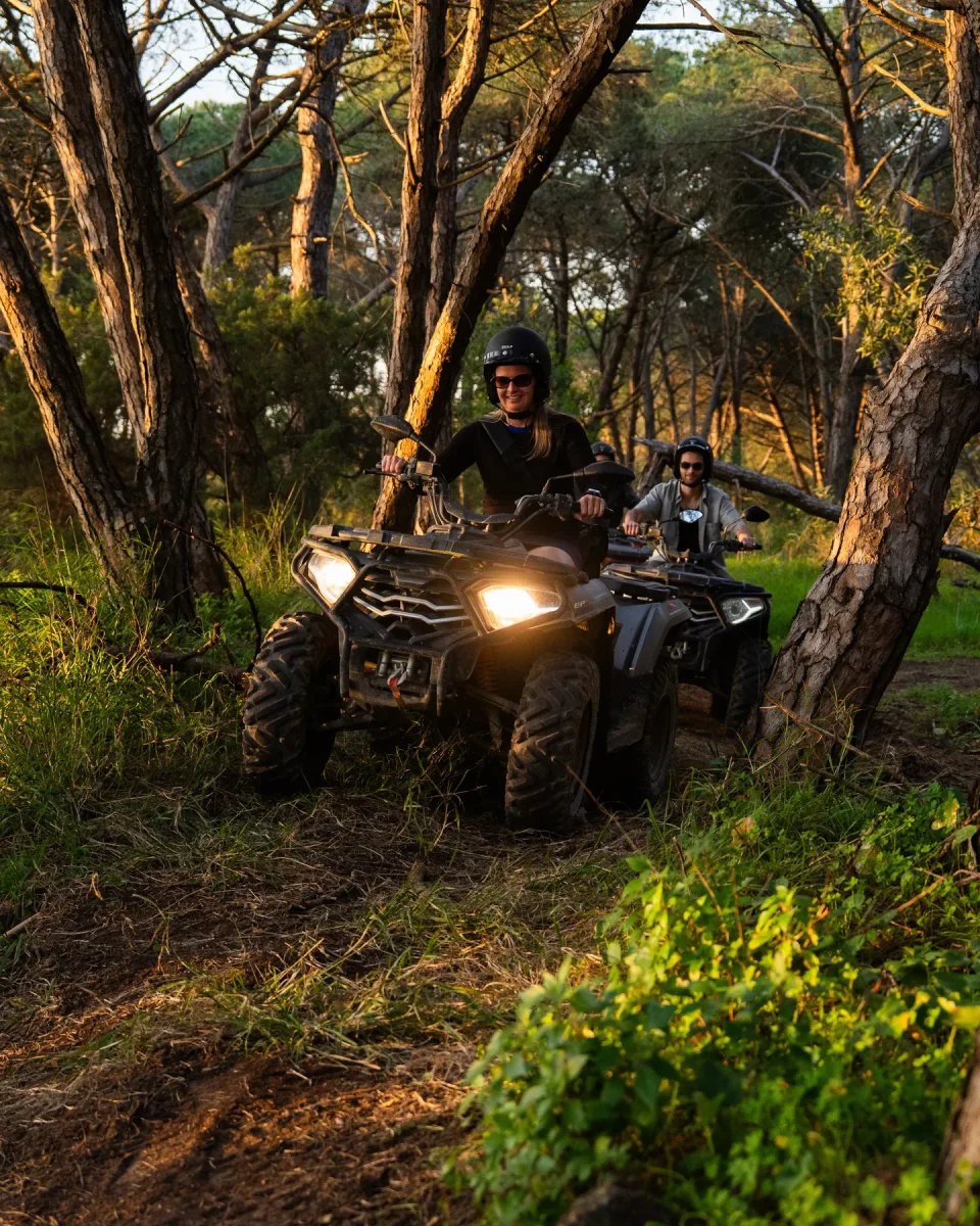 Two quad riders coming through a sunlit pine forest in Costa da Caparica at golden hour