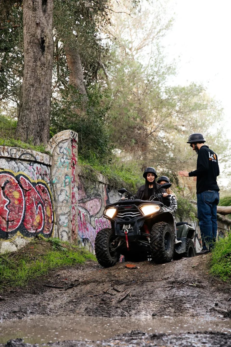 Lx4 guide briefing two quad riders at a graffiti-walled trailhead in Costa da Caparica
